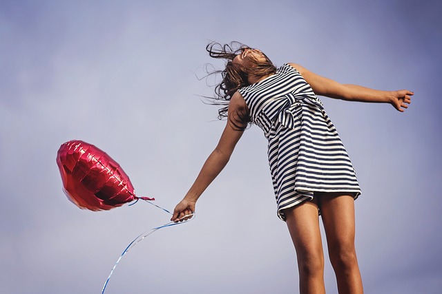 woman jumping in air holding red heart balloon