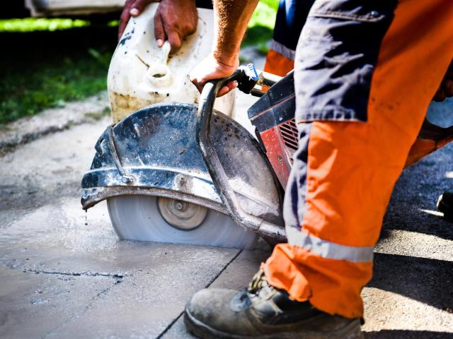 closeup of construction worker cutting concrete with large circular saw