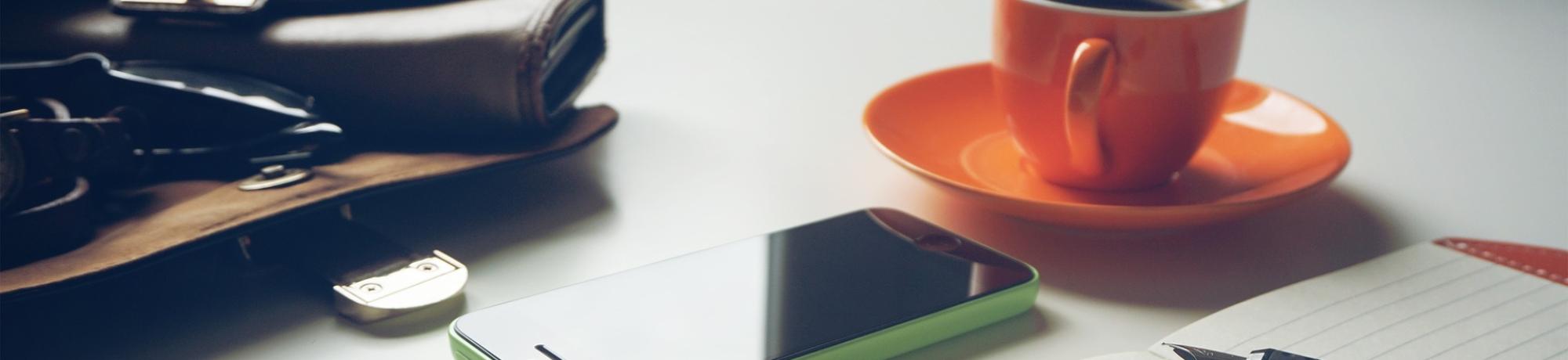 Coffee mug, smart phone, purse and notebook on desk