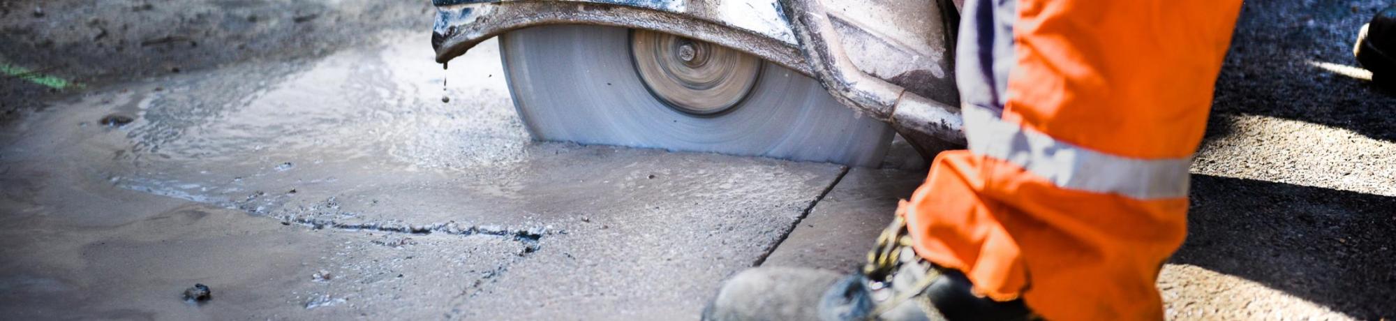 closeup of construction worker cutting concrete with large circular saw